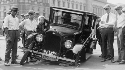 grayscale photo of people standing near the wrecked vintage car