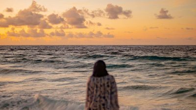 A person walking on a sandy beach toward the ocean under a warm sky