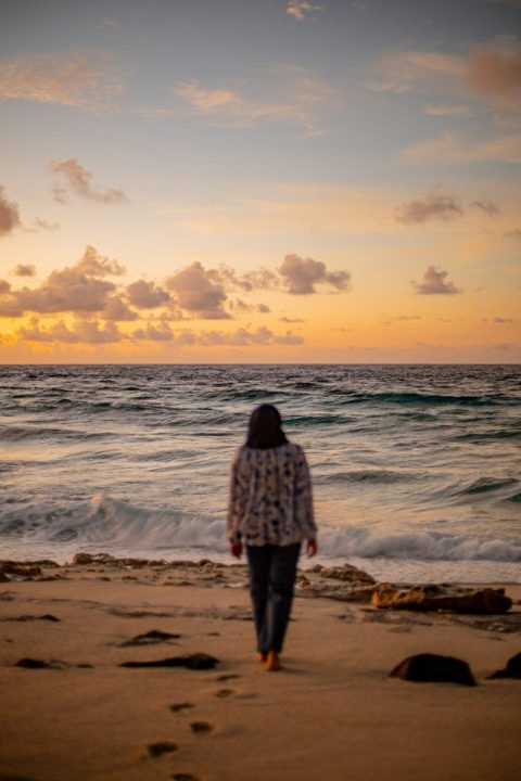 A person walking on a sandy beach toward the ocean under a warm sky