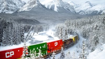 a moving train on a snow covered ground near the snow covered trees and mountains