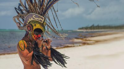 man in tribal costume playing instrument at beach