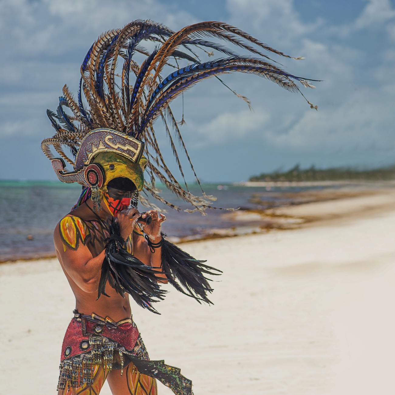 man in tribal costume playing instrument at beach