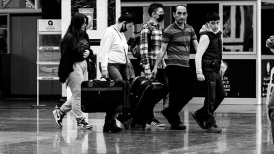 grayscale photo of people carrying luggage while walking