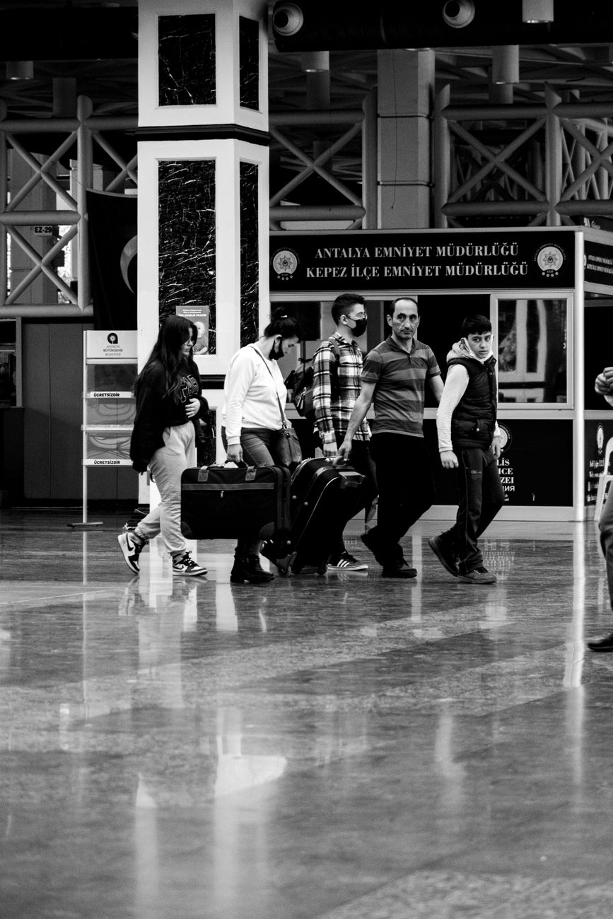 grayscale photo of people carrying luggage while walking