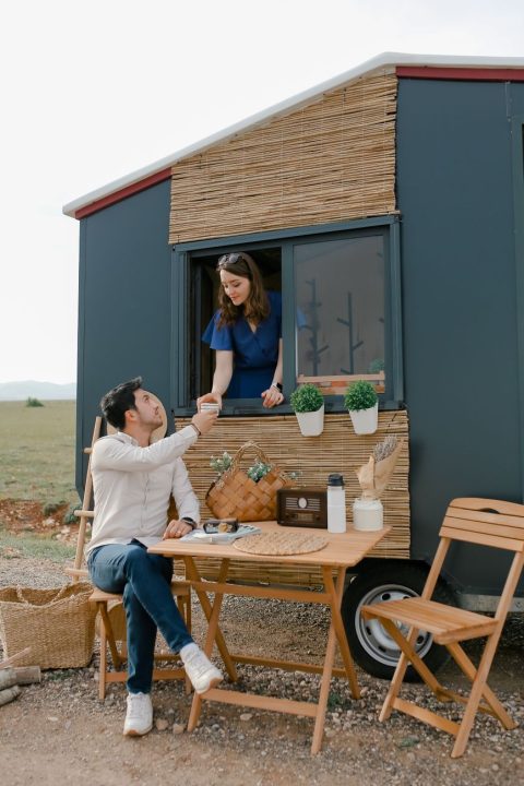 woman serving cup of tea from kitchen window to her partner