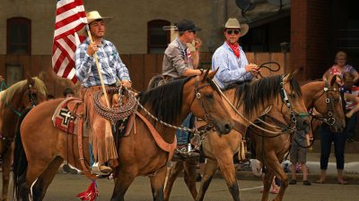 cowboys with flag riding horses on street