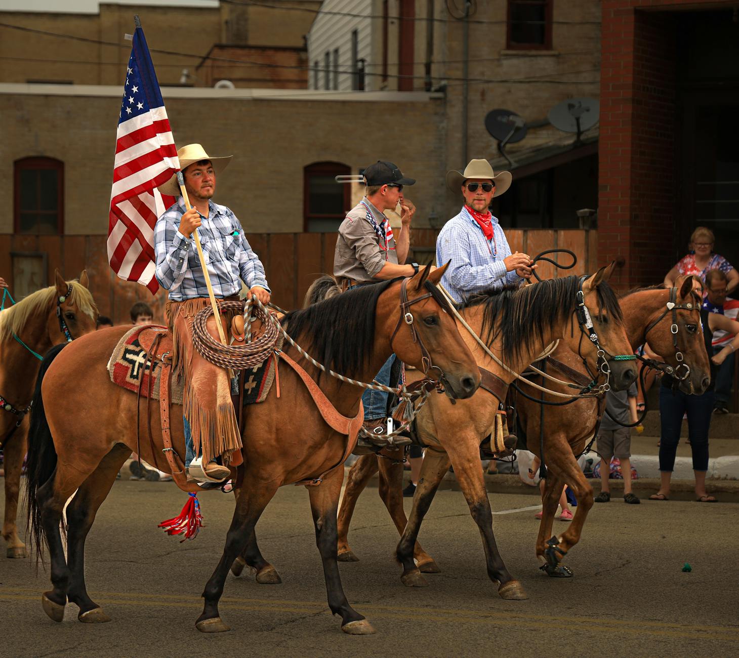 cowboys with flag riding horses on street