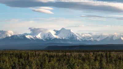 an aerial photography of a snow covered mountains near the green trees under the cloudy sky