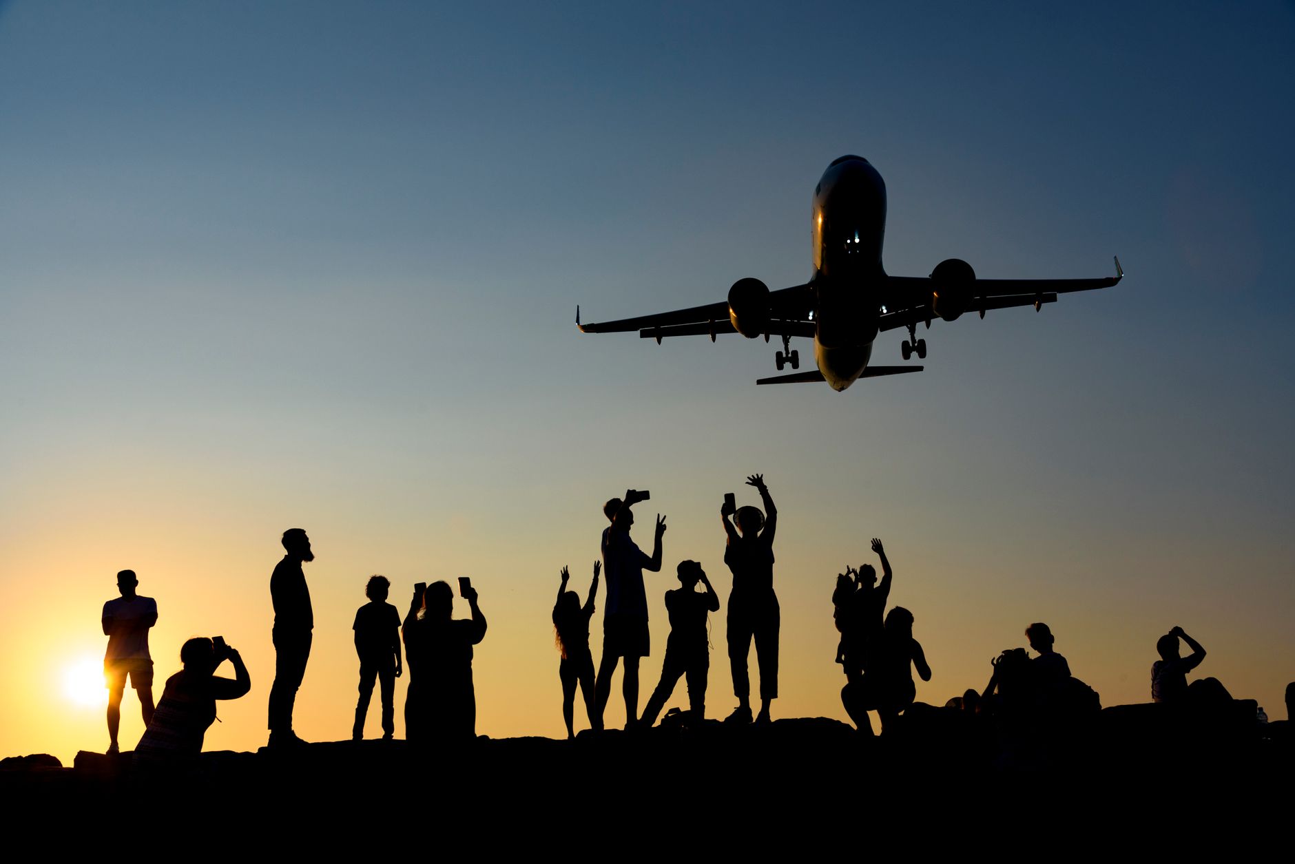 silhouettes of people photographing a plane at sunset