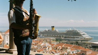 man playing on saxophone in front of town and ship on sea