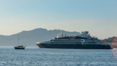 seascape with a large ferry and a small boat against a hill