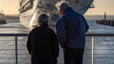 elderly couple in jackets standing by a railing watching a ship