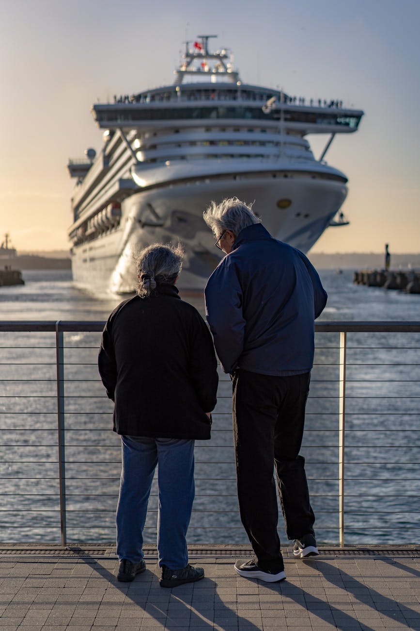 elderly couple in jackets standing by a railing watching a ship