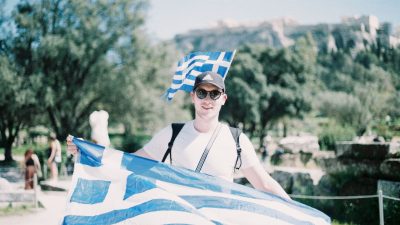 young man in sunglasses holding a greek flag