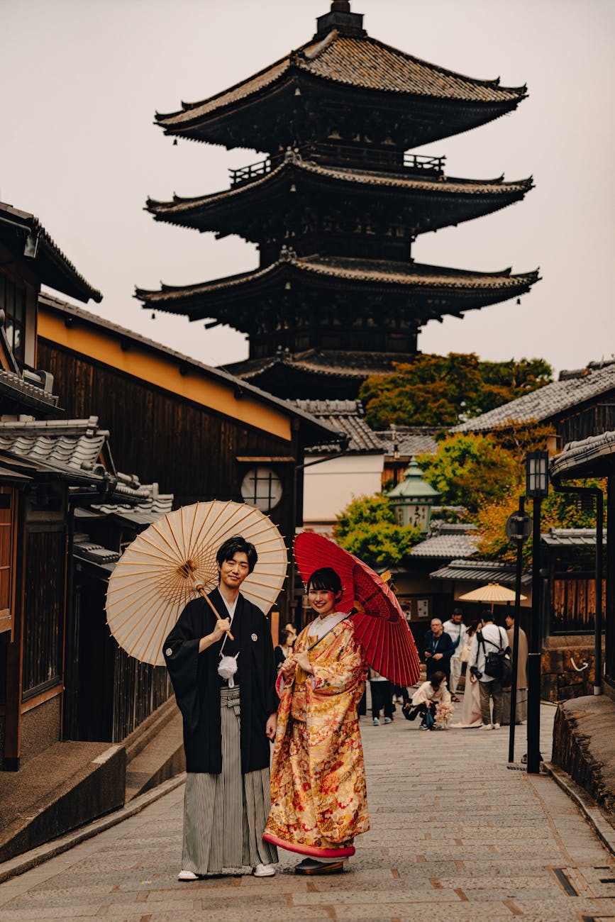 woman and man in traditional clothing posing with pagoda in town behind