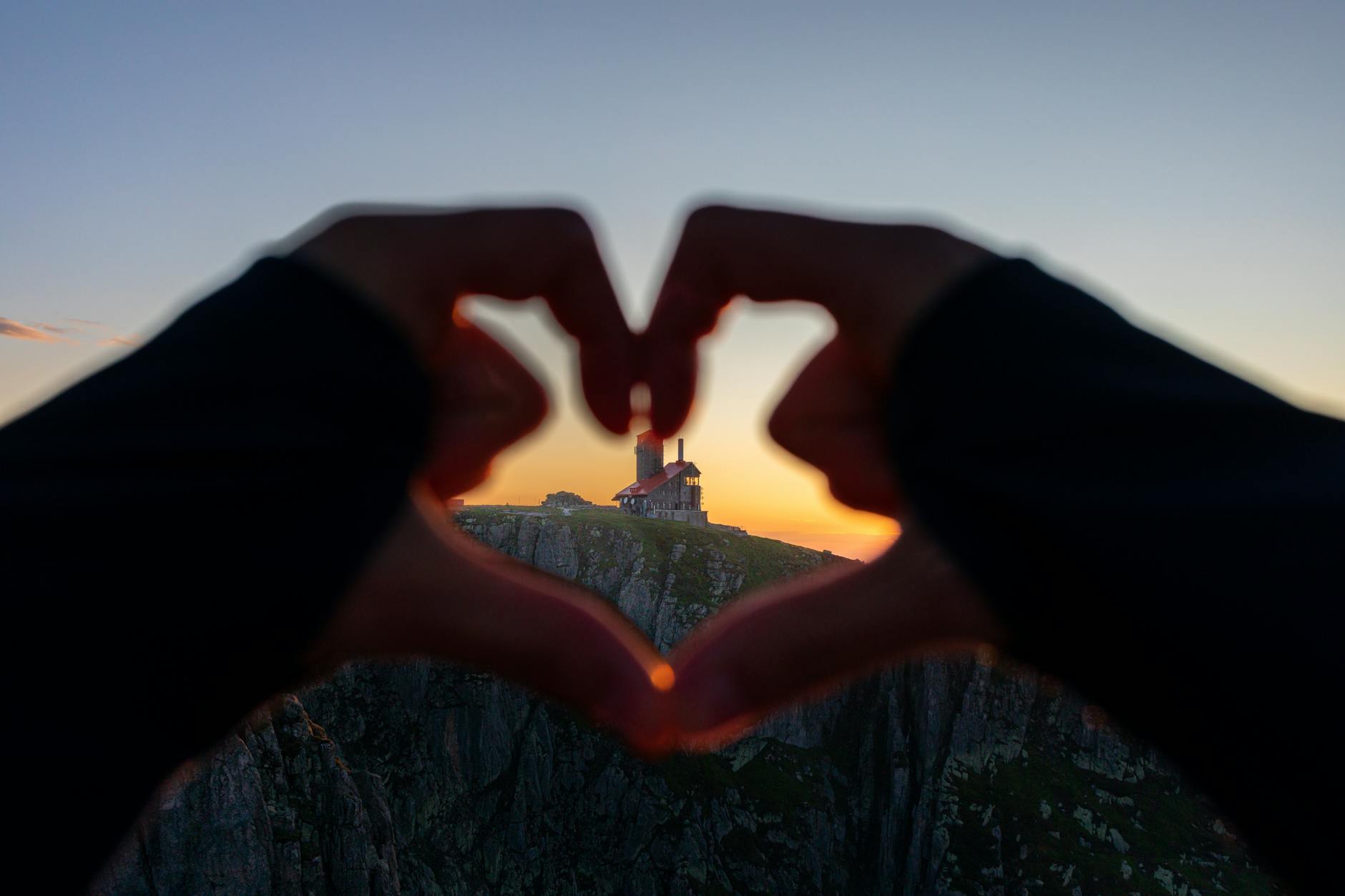 cliff and building behind hands in heart shape at sunset