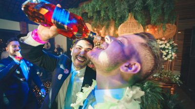 man pouring whiskey from a bottle into another man mouth