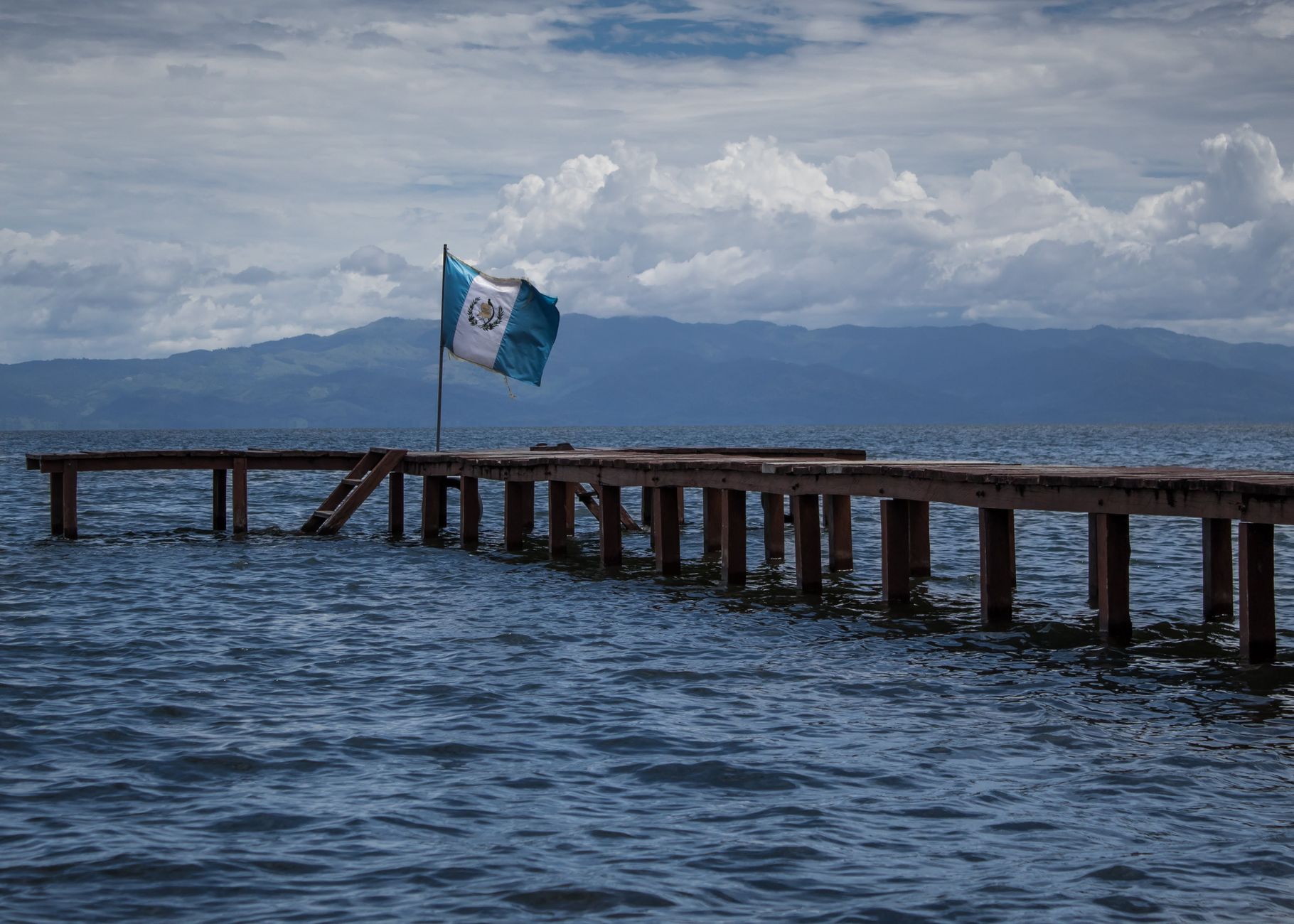 a wooden pier with a flag of guatemala on a body of water