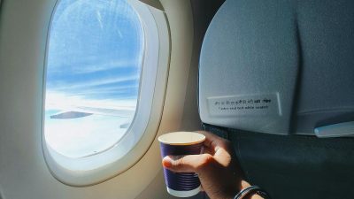 hand holding cup by window of flying airplane