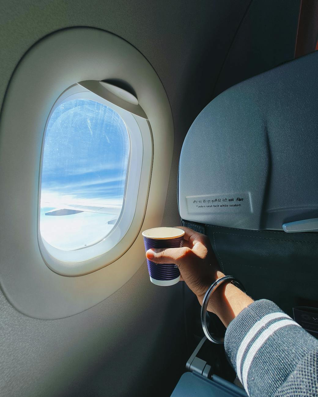 hand holding cup by window of flying airplane