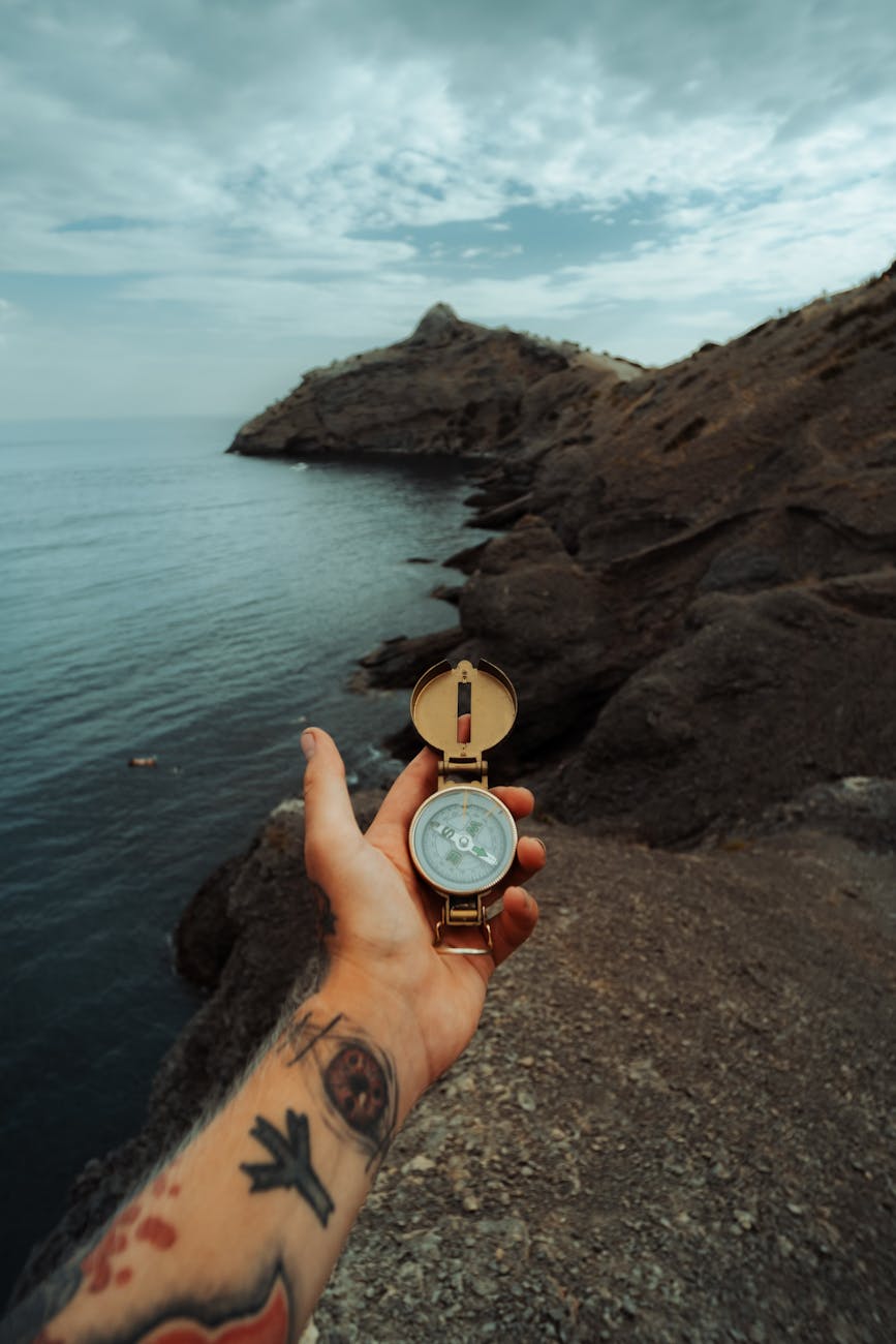 man with tattoos holding a compass at a rocky seashore in crimea ukraine