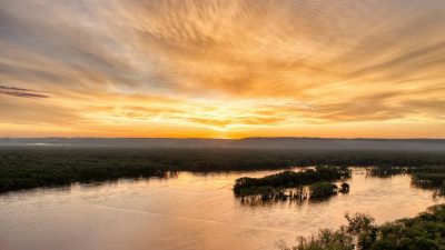 a sunset over a river with trees and water