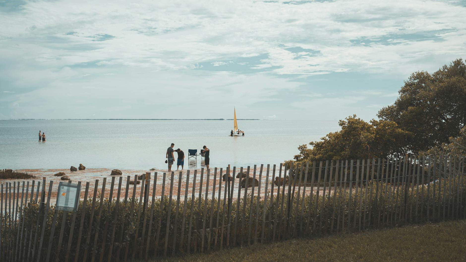 a group of people standing on the beach near a fence