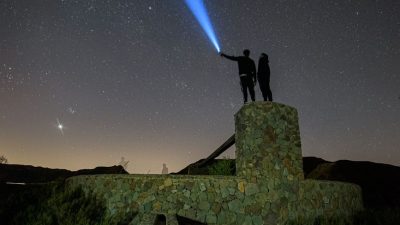 a man and woman standing on top of a hill with a blue light shining