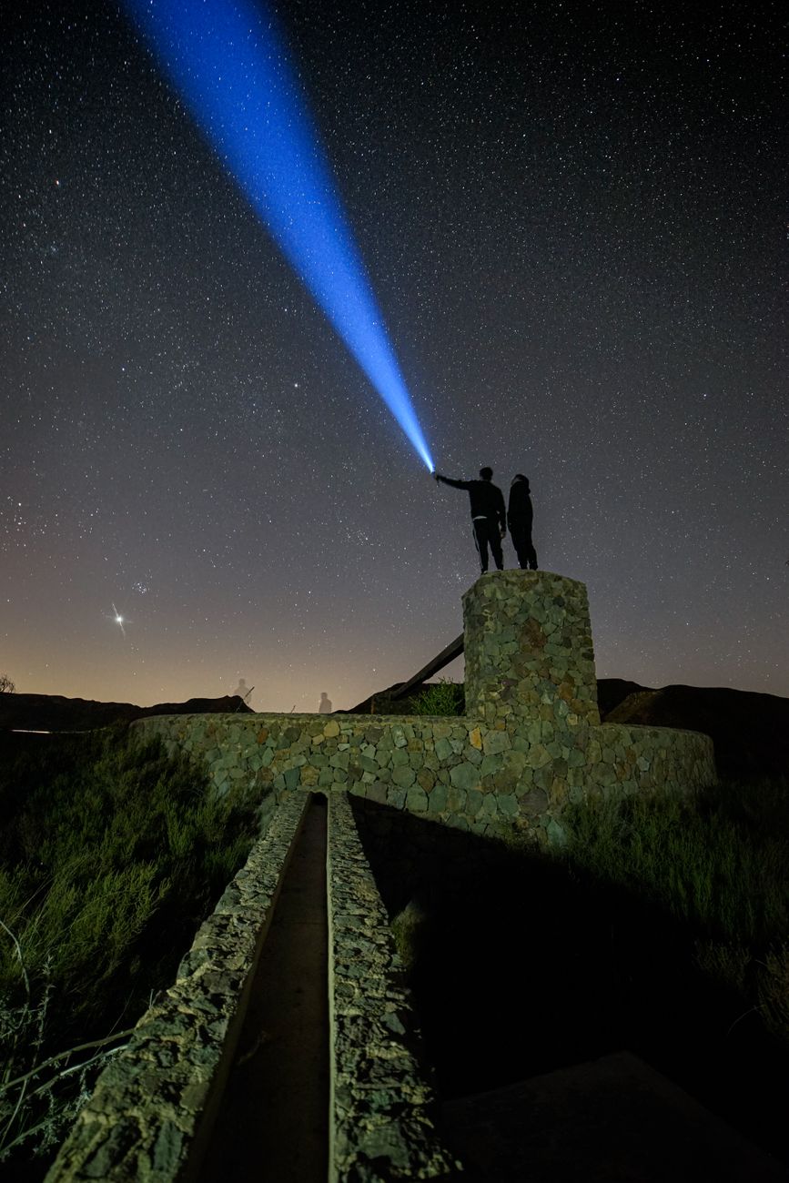 a man and woman standing on top of a hill with a blue light shining