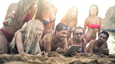 group of friends enjoying tablet on beach