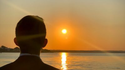 silhouette of man watching sunset over water