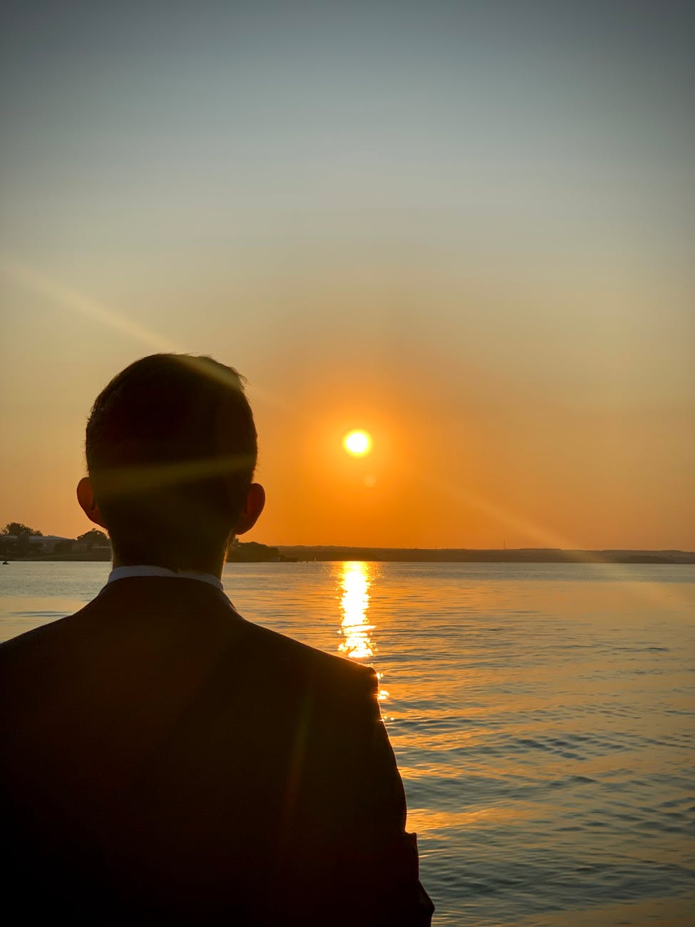 silhouette of man watching sunset over water
