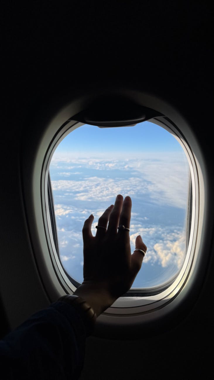 hand reaching through airplane window in flight