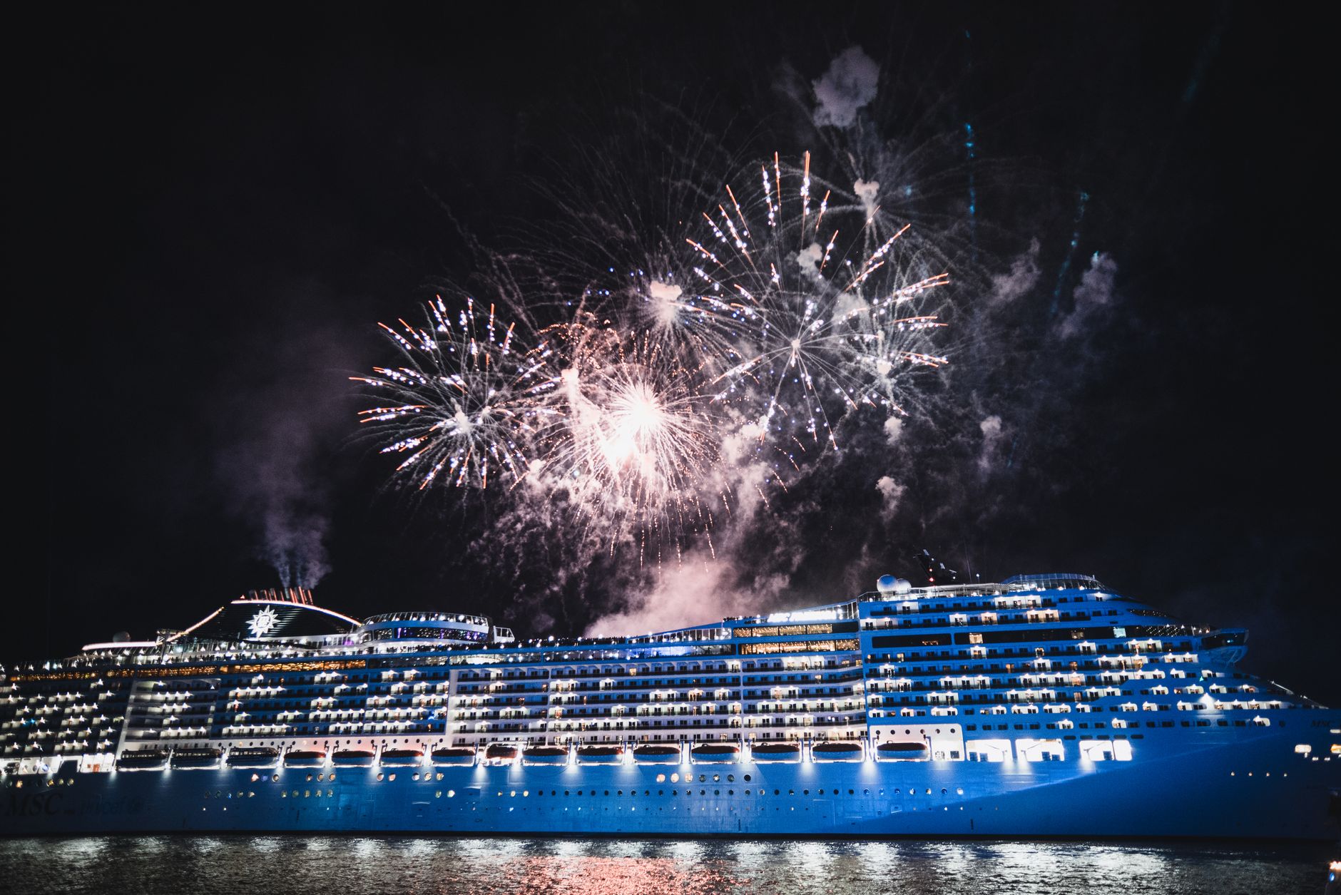 cruise ship illuminated by fireworks at night
