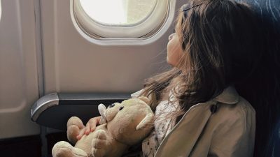 young girl with teddy bear gazing from airplane