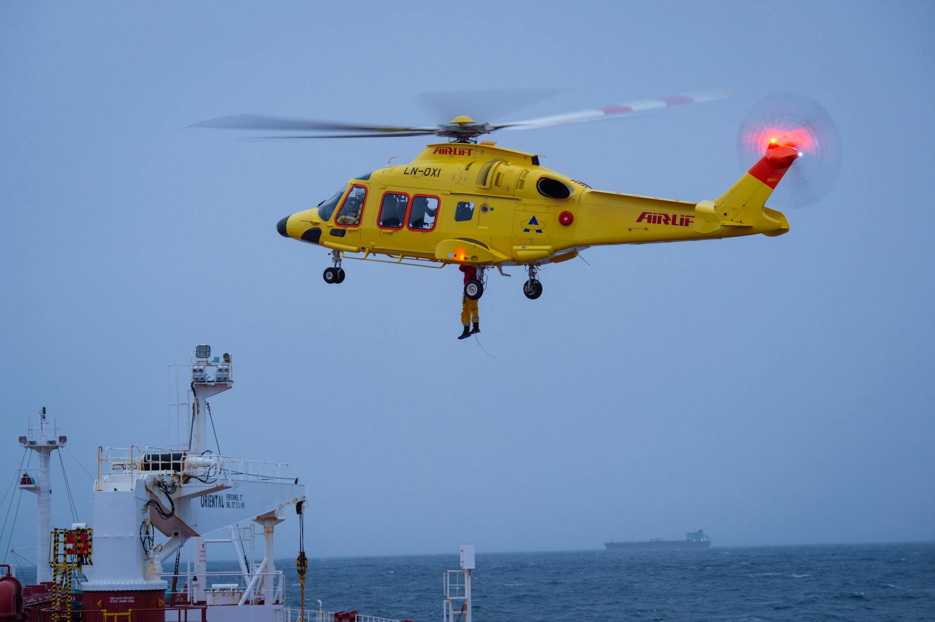 yellow rescue helicopter hovers over vessel at sea
