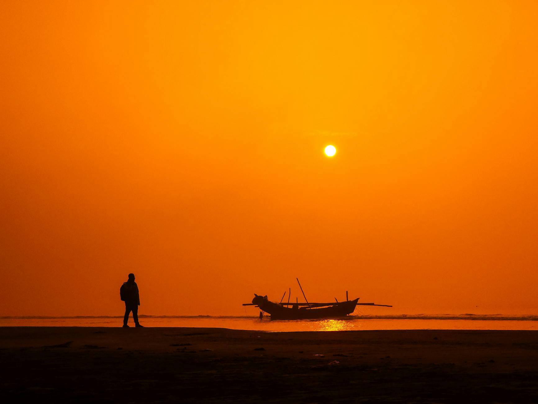 silhouette on beach at sunset with fishing boat