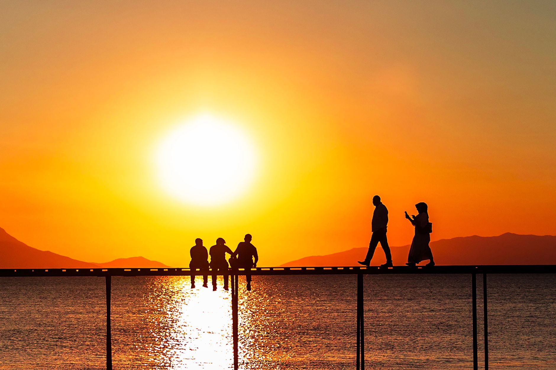 silhouetted people on pier at sunset