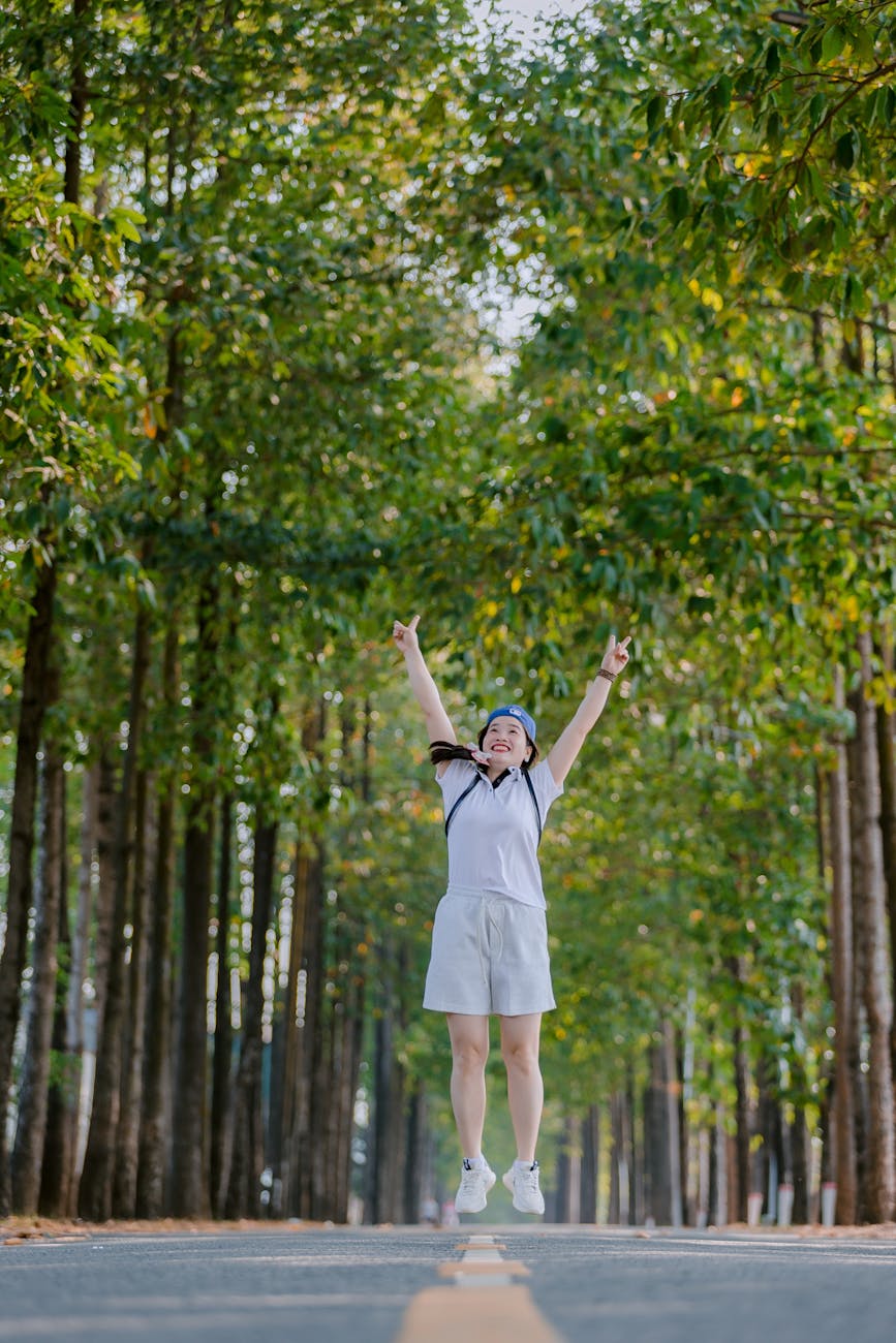 excited woman jumping on tree lined road