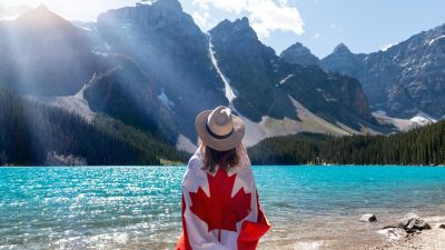 person with a canadian flag around her standing near lake