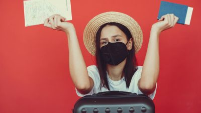 sad woman in respiratory mask with suitcase and passport
