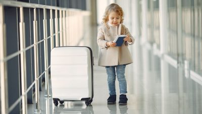 happy little girl with suitcase and passport in airport corridor