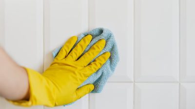 crop person cleaning white tile wall with microfiber cloth