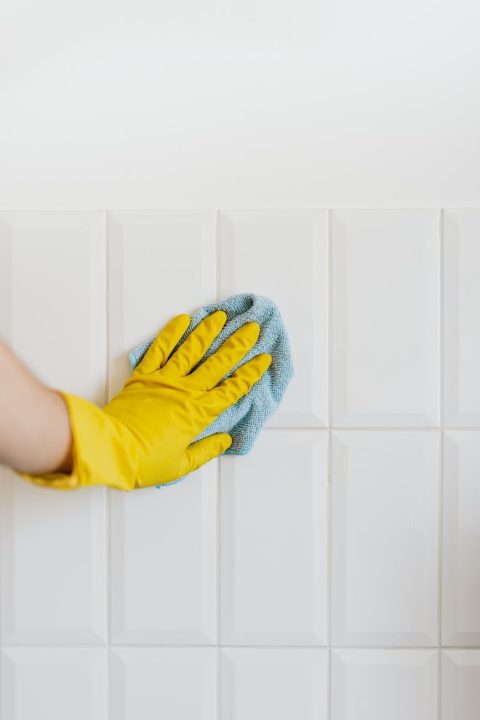 crop person cleaning white tile wall with microfiber cloth
