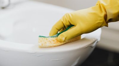 crop person in rubber glove cleaning toilet bowl