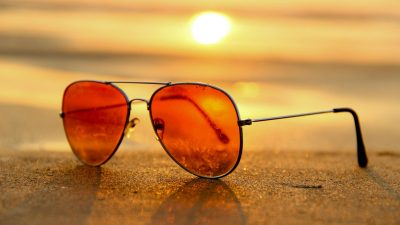 red lens sunglasses on sand near sea at sunset selective focus photography