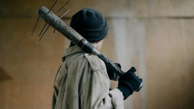 person in black knit cap and beige coat holding brown wooden stick