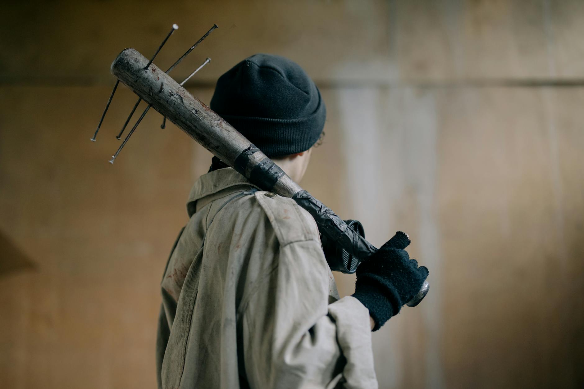 person in black knit cap and beige coat holding brown wooden stick