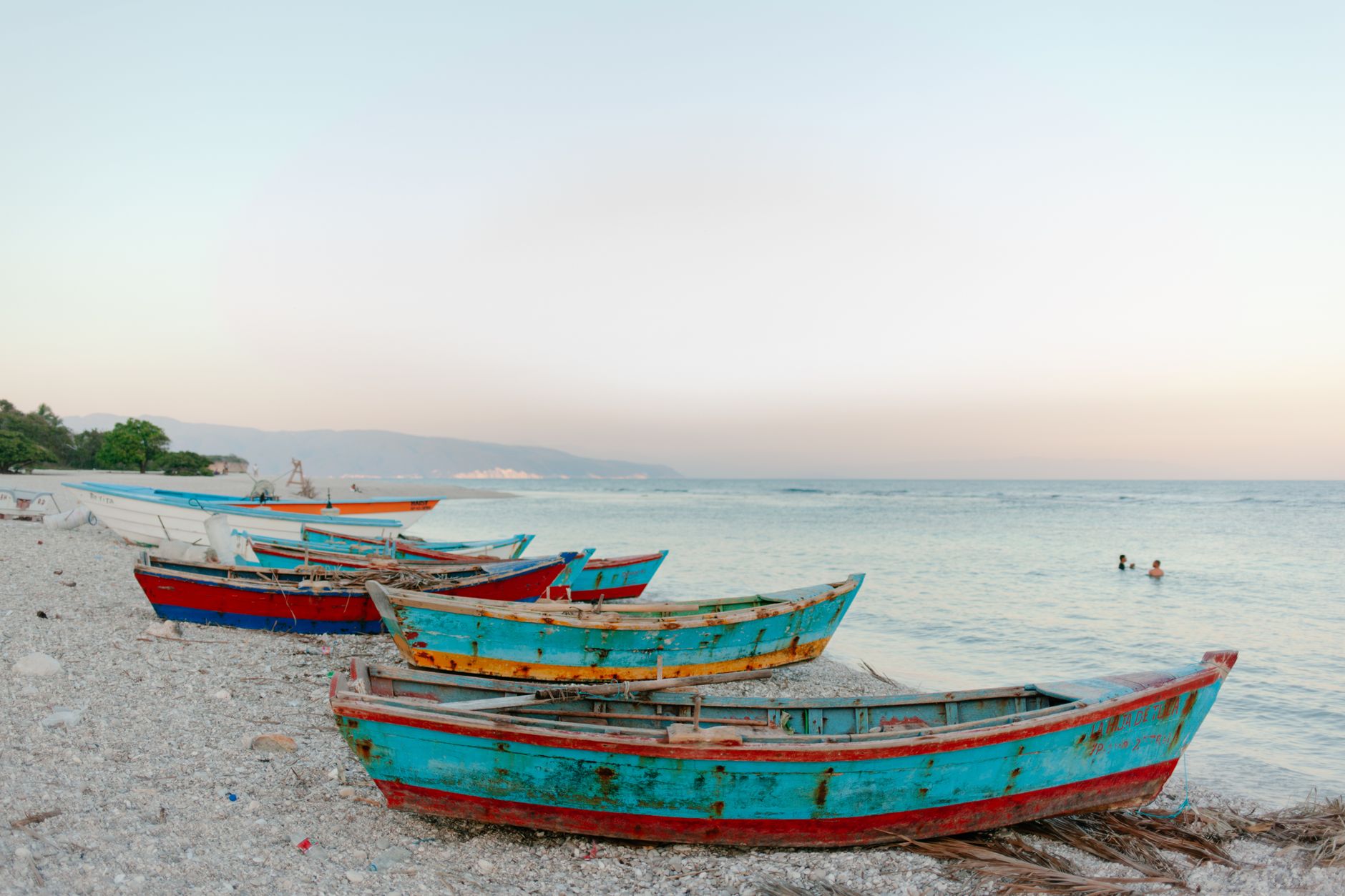 boats on beach near sea with swimming tourists