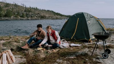 a couple sitting on picnic mat near a tent along a river